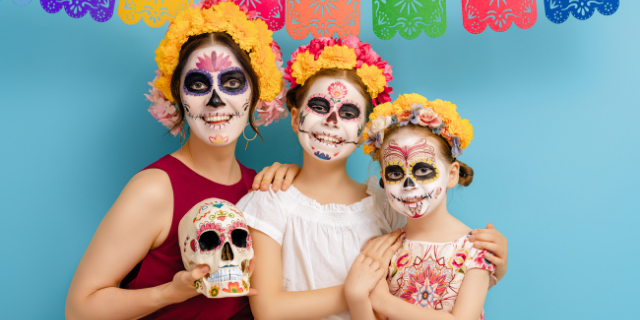Mulher adulta segurando uma caveira mexicana e duas crianças maquiadas para o dia dos mortos