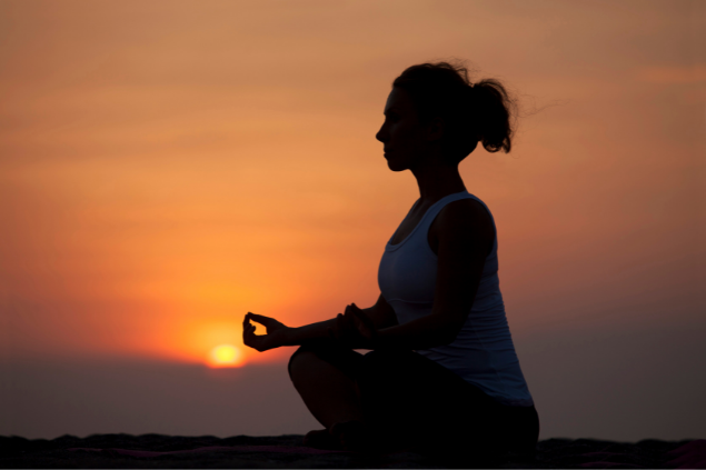 Mulher meditando durante o pôr-do-sol