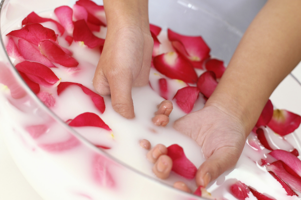 Pessoa mexendo com as mãos em um recipiente com leite e pétalas de rosa