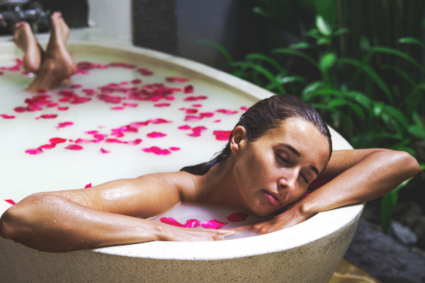Mulher em uma banheira de leite com pétalas de rosa