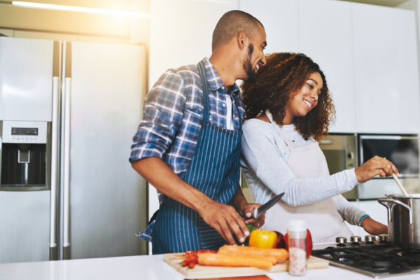 Imagem de um homem e uma mulher cozinhando juntos na cozinha. Os dois estão sorrindo