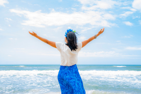 Mulher celebrando Iemanjá na beira do mar com os braços abertos