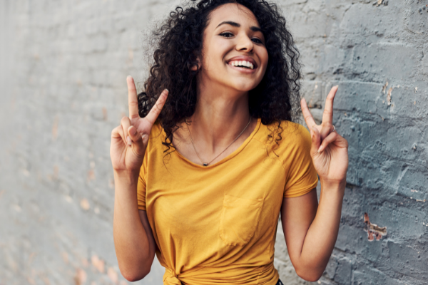 Nicola Katie / Canva Menina feliz fazendo o sinal da paz com a mão