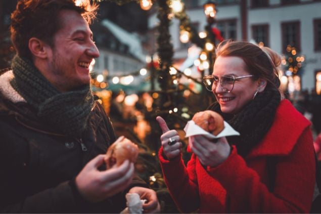 Homem e mulher sorrindo em uma rua enfeitada com acessórios e luzes de natal