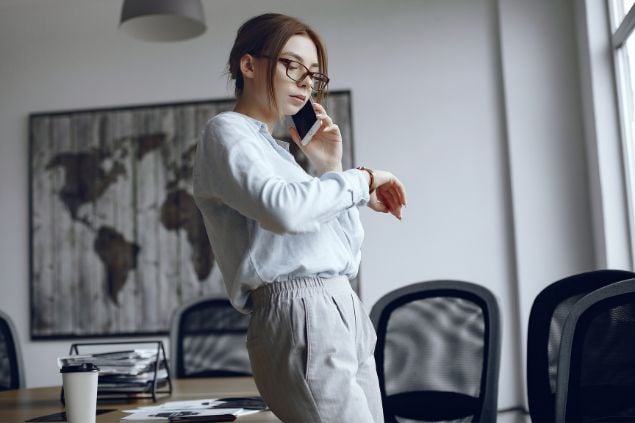 Imagem de uma mulher falando no telefone, olhando para o seu relógio de pulso e com feição de impaciência