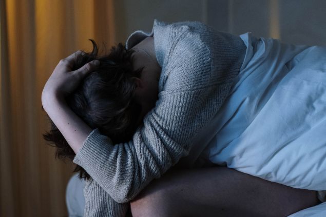 cottonbro de Pexels/ Canva Imagem de uma pessoa com a cabeça baixa e as mãos na cabeça sentada na cama como se estivesse preocupada