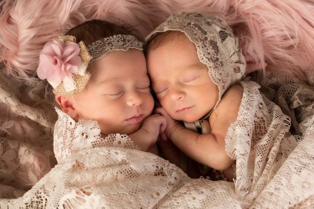 Imagem de duas bebês gêmeas na cama enroladas em um pano bordado