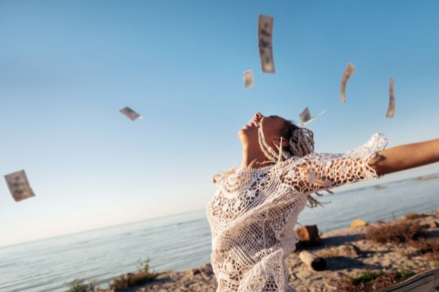 Imagem de uma mulher sorrindo com os braços abertos ao ar livre e notas de dinheiro caindo ao redor dela