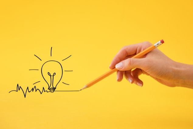 Imagem da mão de uma pessoa com um lápis desenhando uma lâmpada em um fundo amarelo