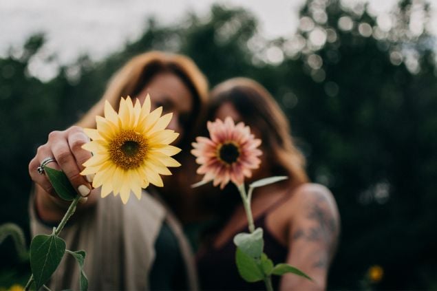Imagem de duas mulheres segurando cada uma, uma flor na frente delas 