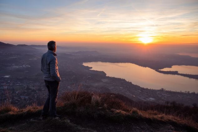 Imagem de um homem olhando ao horizonte em cima de uma montanha ao pôr-do-sol