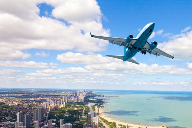 Imagem de um avião decolando por cima de uma praia e prédios