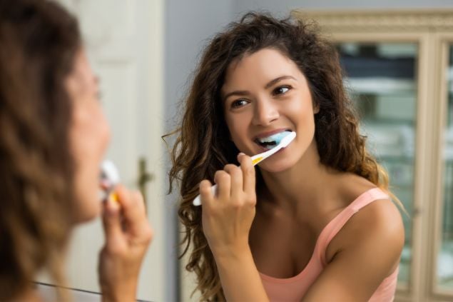 Imagem de uma mulher de frente para o espelho e escovando os dentes
