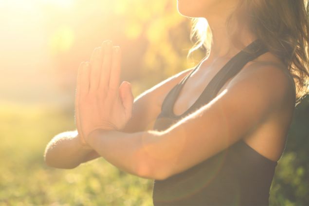 Imagem de uma mulher com as mãos em posição de oração e o sol a iluminando