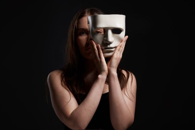 Imagem de uma mulher em um fundo preto tirando uma máscara branca
