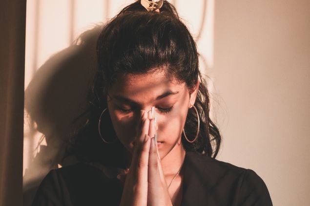 Imagem de uma mulher com as mãos juntas em oração e os olhos fechados