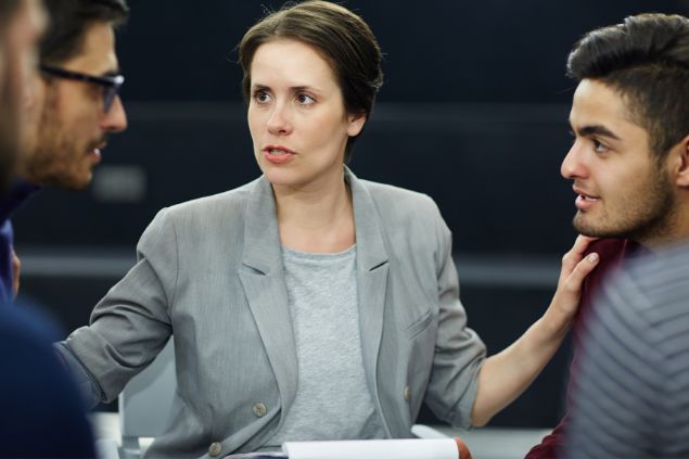 Imagem de uma mulher tentando apartar uma discussão entre dois rapazes no local de trabalho