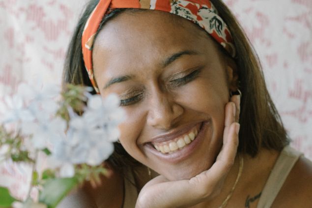 Imagem de uma mulher sorrindo de olhos fechados e com flores na mão