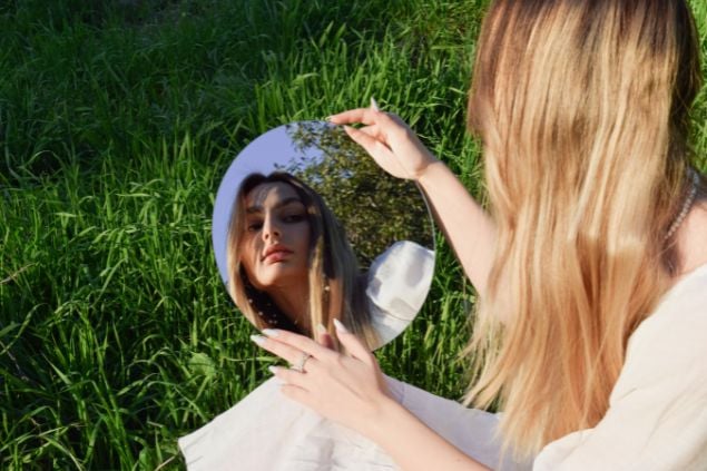 Imagem de uma mulher se olhando no espelho sentada na grama