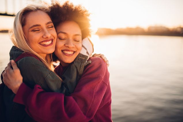 Imagem de duas mulheres se abraçando e sorrindo e o sol refletido atrás delas