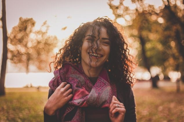 Imagem de uma mulher sorrindo com os cabelos ao vento ao ar livre