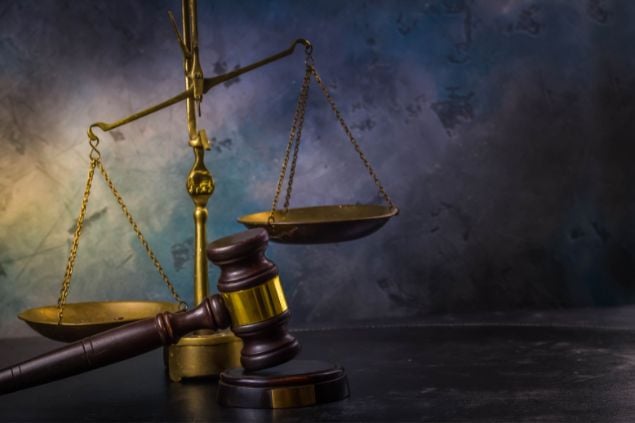Objeto balança de justiça em cima de uma mesa, e ao lado o martelo em que se dá o veredito final