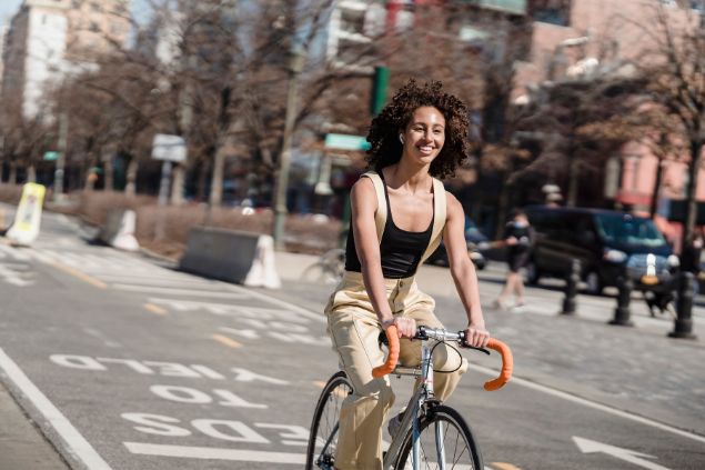 Mulher andando de bicicleta pela cidade com sorriso no rosto