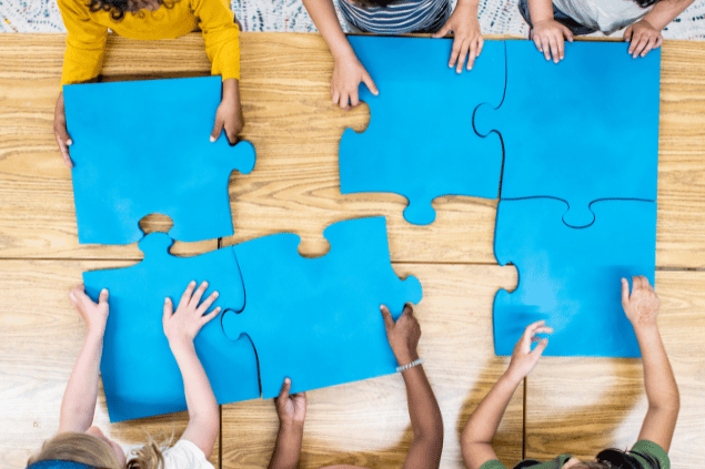 Crianças se ajudando a montar um quebra-cabeça gigante. 