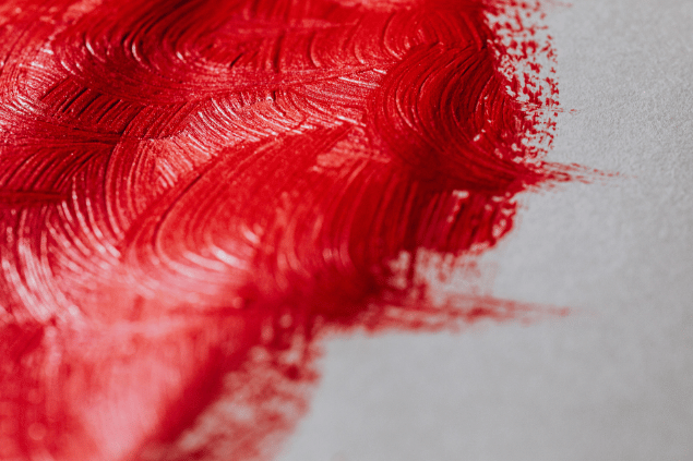 Pinceladas espessas de tinta vermelha sobre uma superfície clara, mostrando textura e movimento das cerdas do pincel.