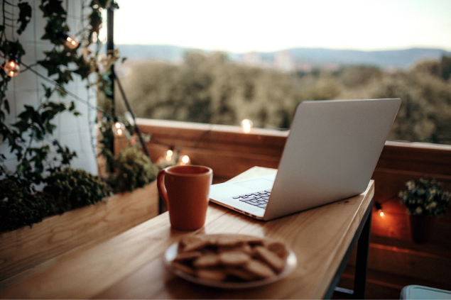 Um laptop em cima de uma mesa de madeira e ao lado de uma xícara com bedida