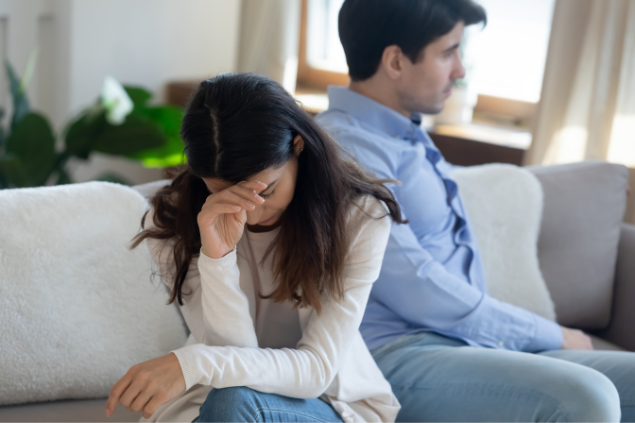 Mulher sentada no sofá com a mão na cabeça demonstrando preocupação junto a seu marido