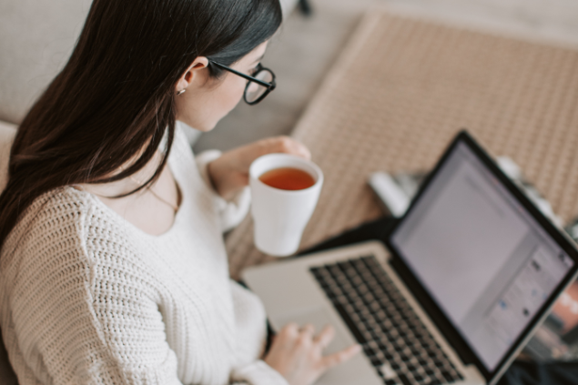 Mulher tomando chá enquanto mexe no notebook