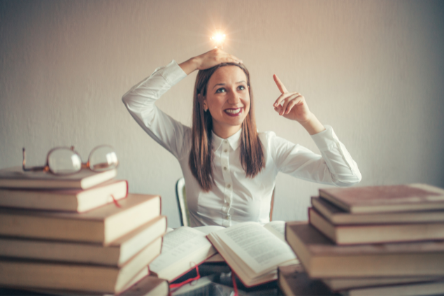 Mulher cercada de livros com uma lâmpada acesa na cabeça