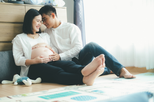 Casal sentado no chão do quarto do novo bebê: a mulher está grávida.