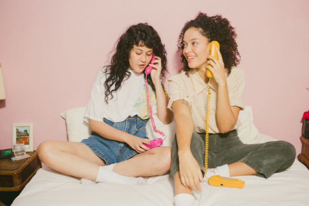 Duas mulheres sentadas na cama falando ao telefone
