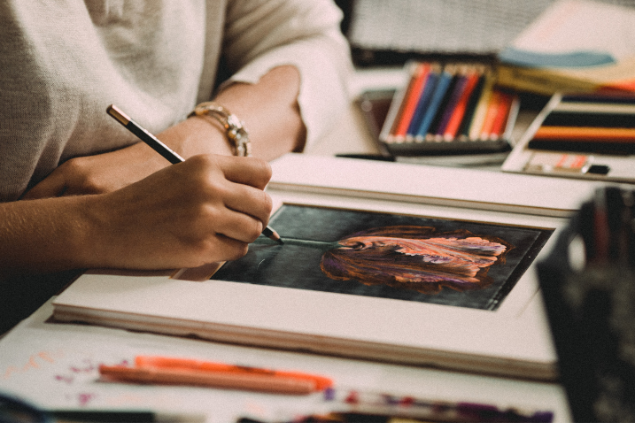 Mulher desenhando em mesa cheia  de lápis de cores