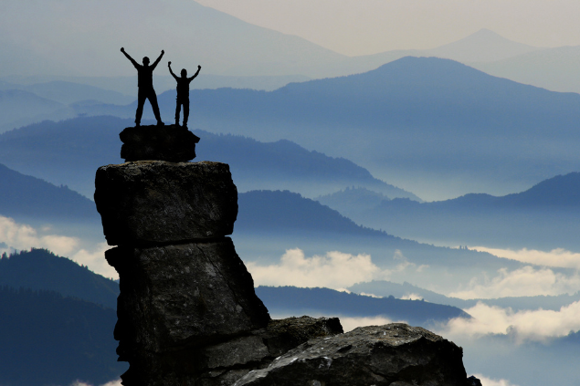 Duas pessoas em cima de uma pedra, com os braços levantados