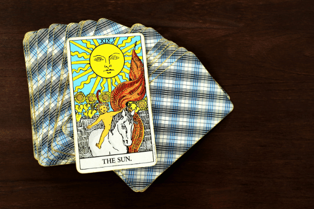 A carta O Sol do Tarot está no foco da imagem. Embaixo dela, há um baralho de cartas.