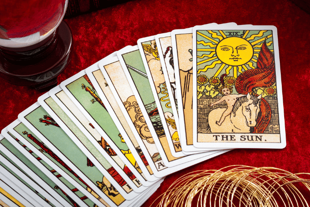 Um baralho de cartas de Tarot está disposto em uma mesa. A carta O Sol está em destaque na imagem.