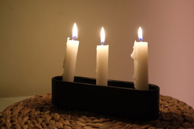 Imagem de três velas brancas acesas. Um dos elementos de oferendas utilizado no ritual para o Pai Benedito da Umbanda.