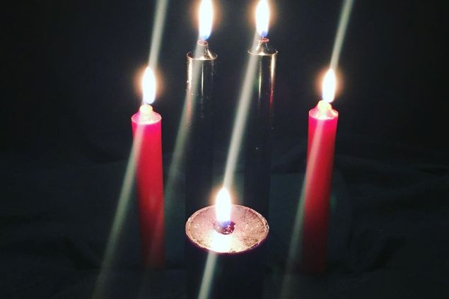 Imagem de algumas velas de cores escuras acesas, simbolizando um dos itens de oferendas para o Exu do Lodo.