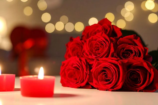 Imagem de um ramalhete de rosas vermelhas, ao lado duas velas vermelhas acesas, simbolizando um dos tipos de oferendas para a Pombagira Sete Saias.