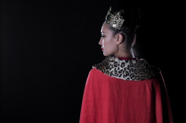 Imagem de uma mulher usando uma capa vermelha com uma gola de tigre. Na cabeça usa uma coroa, simbolizando a pombagira Rainha.