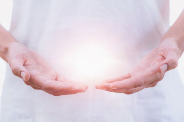 Imagem das mãos de uma pessoa, com uma luz de energia. Ela está aplicando o reiki à distância.