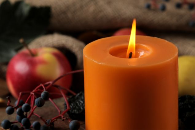 Kristina Maksymova / Getty Images / Canva Imagem de uma vela na cor laranja e vários tipos de frutas, simbolizando uma oferenda para a orixá Egunitá da Umbanda.