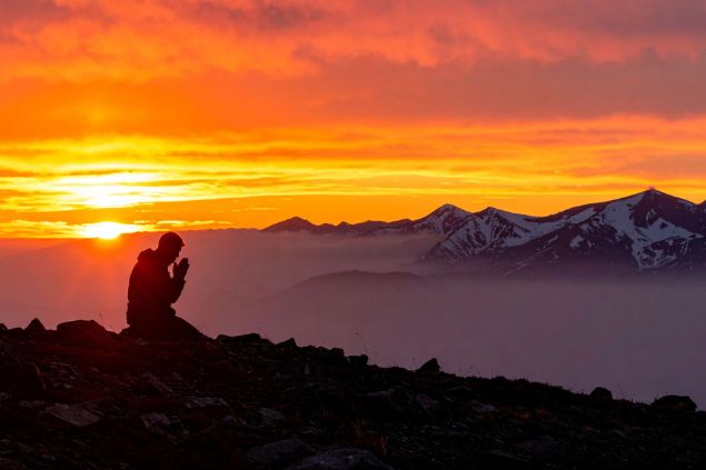 Imagem da silhueta de um homem orando e um lindo pôr do Sol ao fundo.