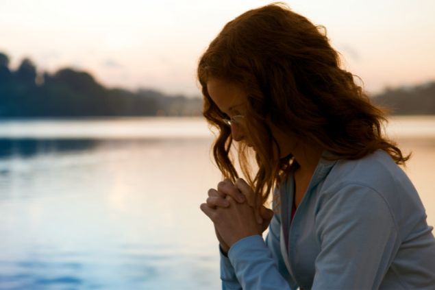 Jjneff / Getty Images Signature / Canva Imagem de uma mulher fazendo uma oração e ao fundo, um lindo lago azul.