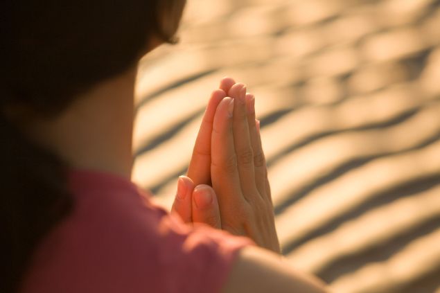 Aflo Images de アフロ(Aflo)/ Canva Imagem de uma mulher em pé, fazendo a sua oração.