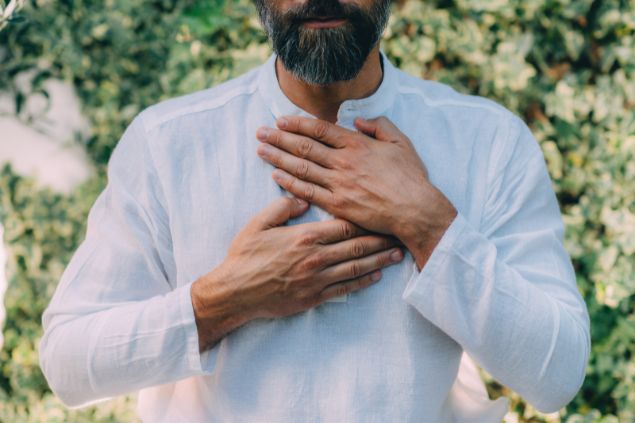 Imagem de um homem de camisa branca com as mãos sobre o peito, simbolizando o sinal de gratidão, um dos princípios do Reiki.
