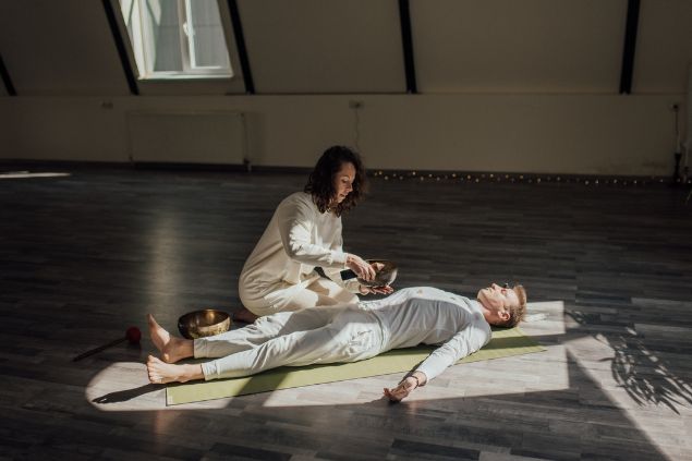 Imagem de uma reikiana aplicando o reiki nos chakras de um paciente deitando sobre o chão em um tapete.